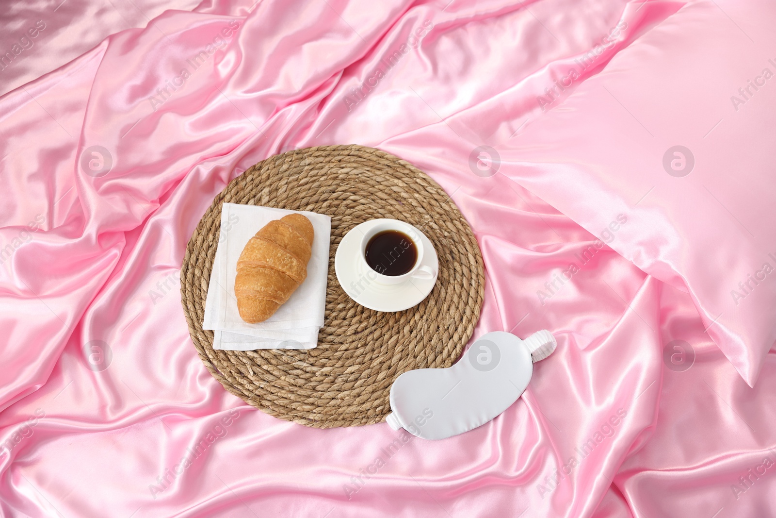 Mat with coffee, croissant and sleep mask on silk bed linens, above view Photo of Mat with coffee, croissant and sleep mask on silk bed linens, above view