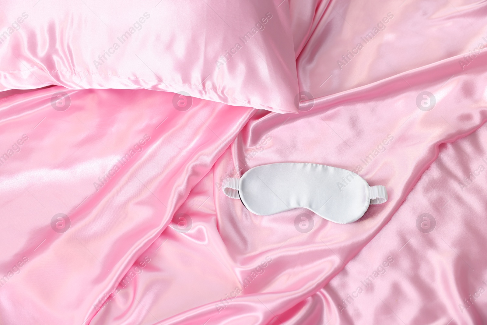 Luxury pink silk linens and sleep mask on bed, top view Photo of Luxury pink silk linens and sleep mask on bed, top view