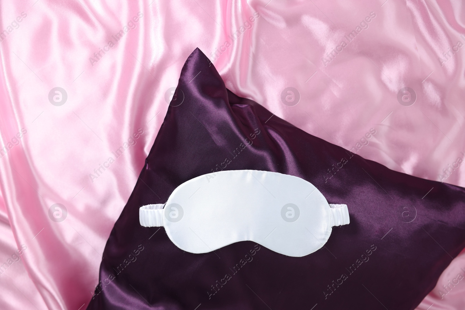 Luxury pink silk linens, pillow and sleep mask on bed, top view Photo of Luxury pink silk linens, pillow and sleep mask on bed, top view