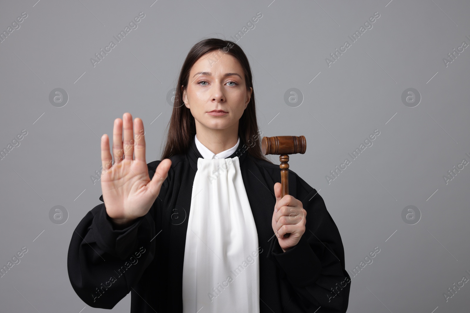 Judge with mallet showing stop gesture on gray background Photo of Judge with mallet showing stop gesture on gray background
