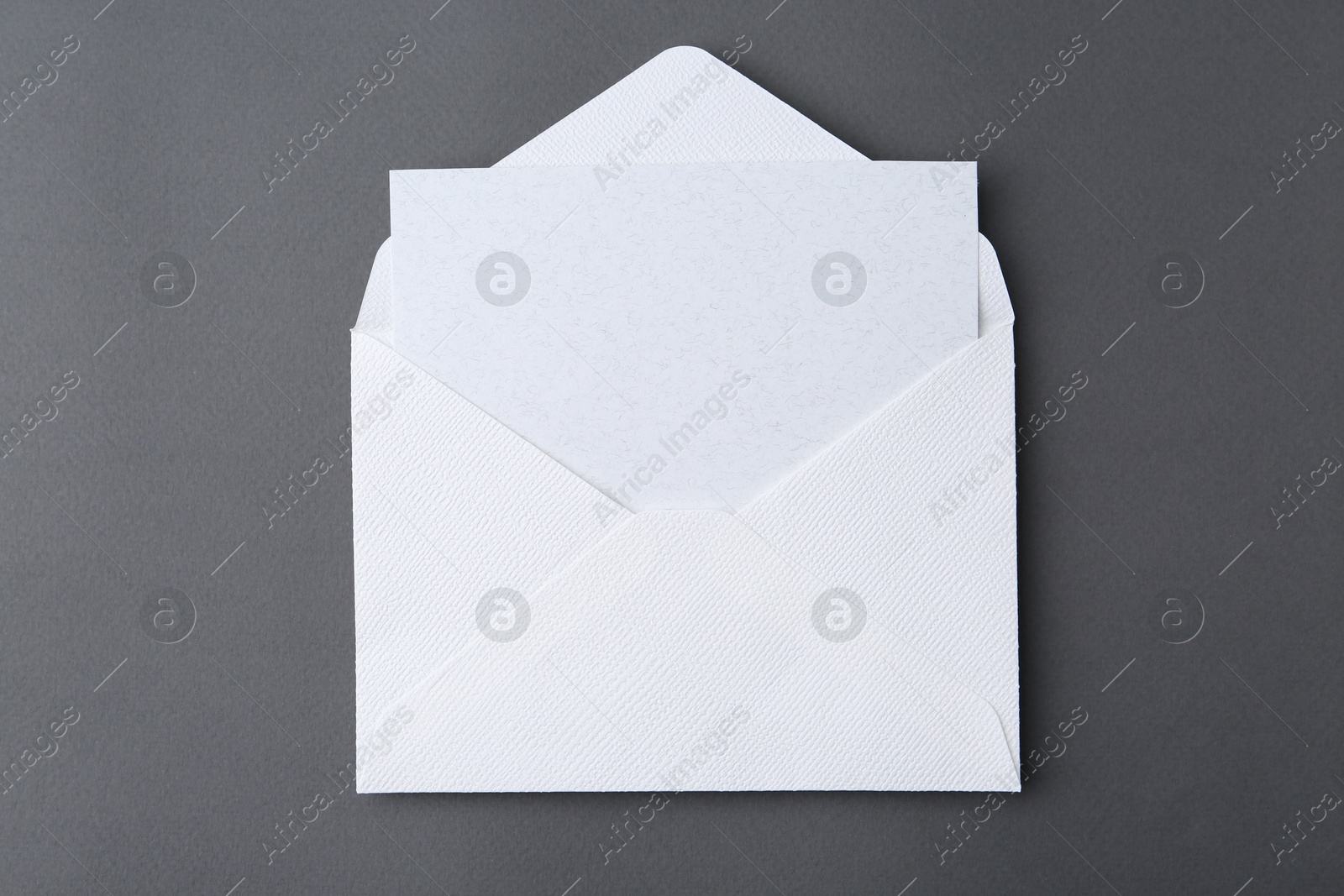 Photo of Blank greeting card in paper envelope on dark grey background, top view