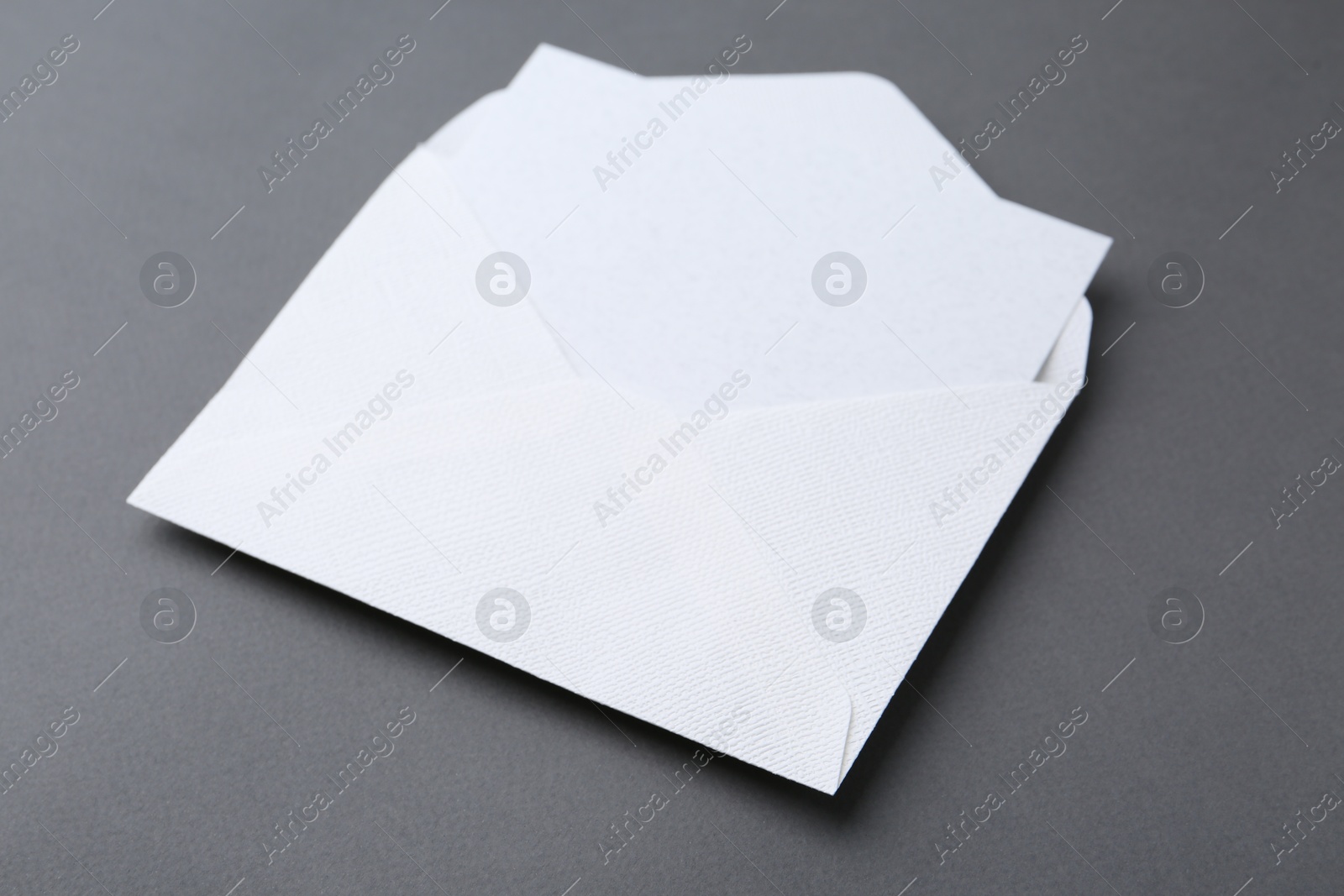Photo of Blank greeting card in paper envelope on dark grey background, closeup