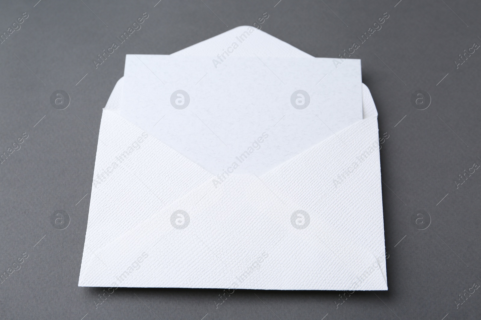 Photo of Blank greeting card in paper envelope on dark grey background, closeup