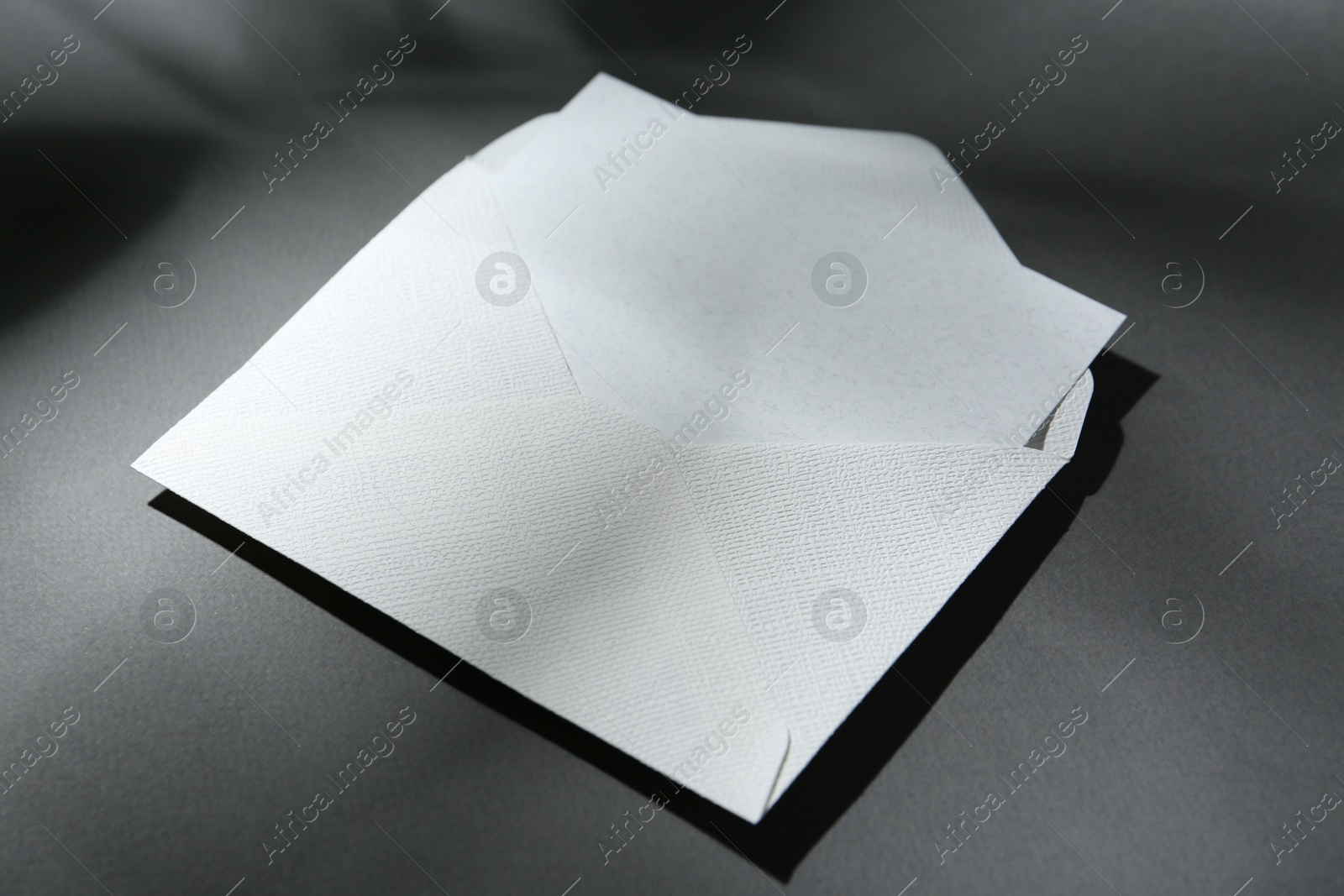 Photo of Blank greeting card in paper envelope on dark grey background, closeup