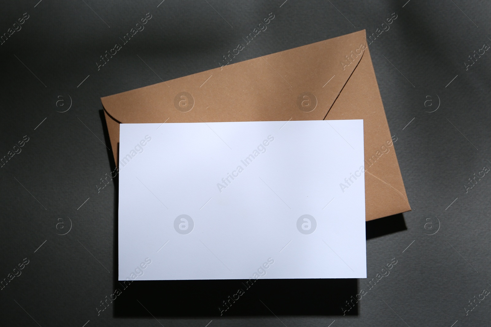 Photo of Blank greeting card and paper envelope on dark grey background, top view