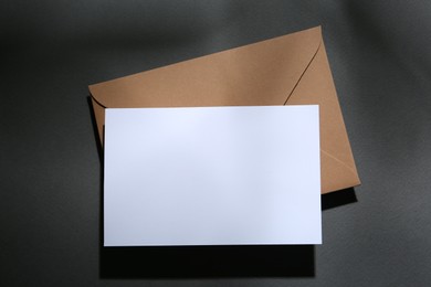 Photo of Blank greeting card and paper envelope on dark grey background, top view