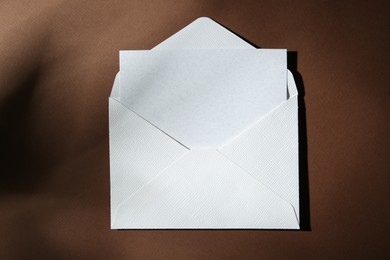 Photo of Blank greeting card in paper envelope on brown background, top view