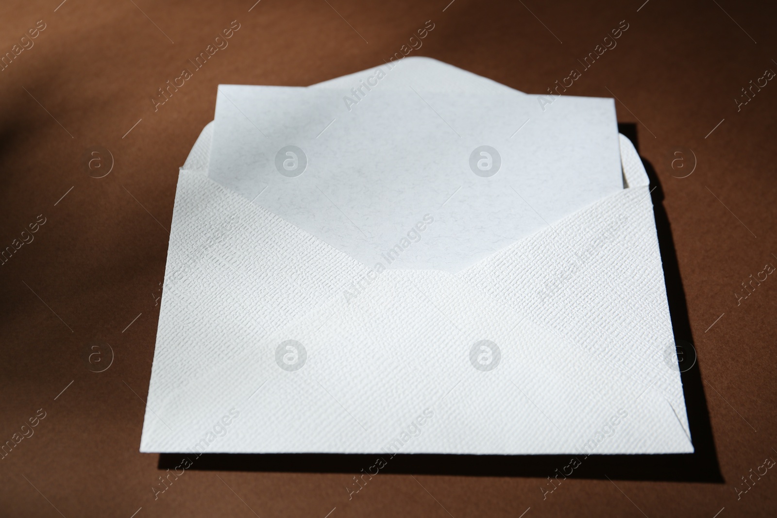 Photo of Blank greeting card in paper envelope on brown background, closeup