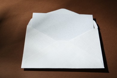 Photo of Blank greeting card in paper envelope on brown background, closeup