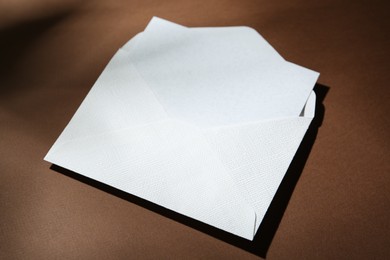 Photo of Blank greeting card in paper envelope on brown background, closeup