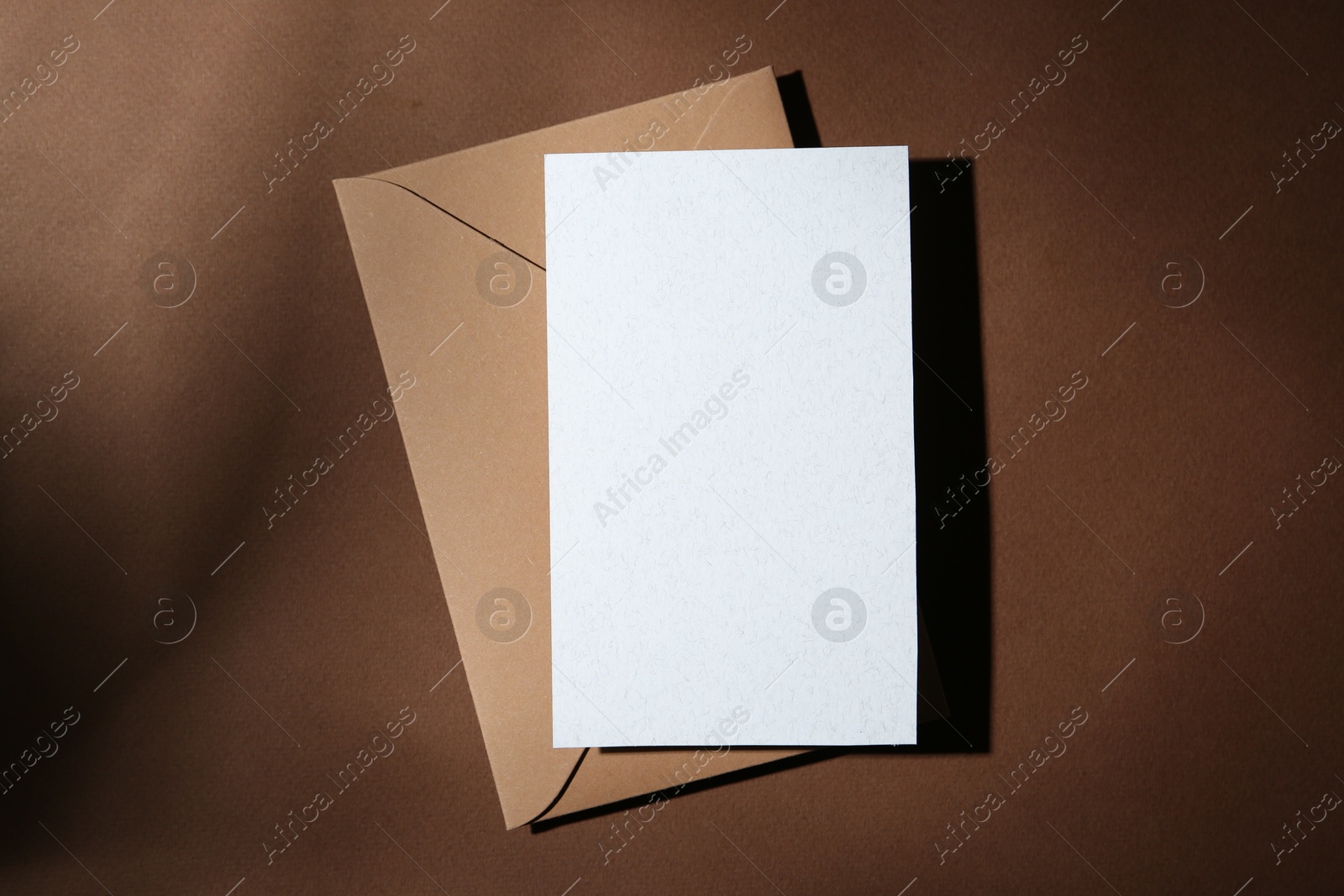 Photo of Blank greeting card and paper envelope on brown background, top view