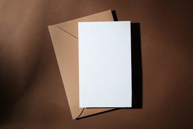 Photo of Blank greeting card and paper envelope on brown background, top view