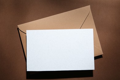 Photo of Blank greeting card and paper envelope on brown background, top view