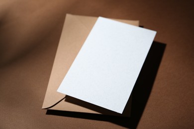 Photo of Blank greeting card and paper envelope on brown background, closeup