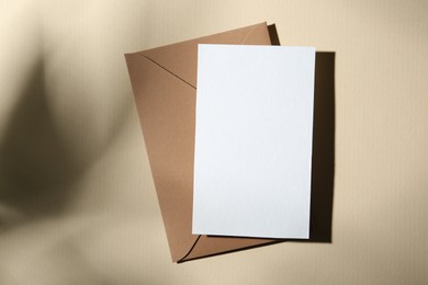 Photo of Blank greeting card and paper envelope on beige background, top view