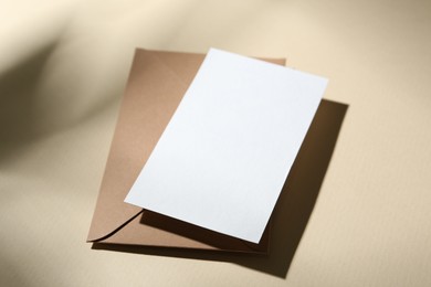 Photo of Blank greeting card and paper envelope on beige background, closeup