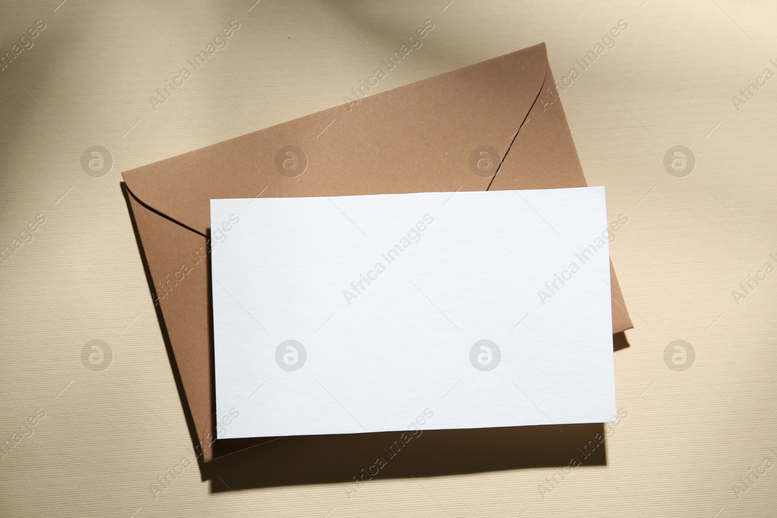 Photo of Blank greeting card and paper envelope on beige background, top view
