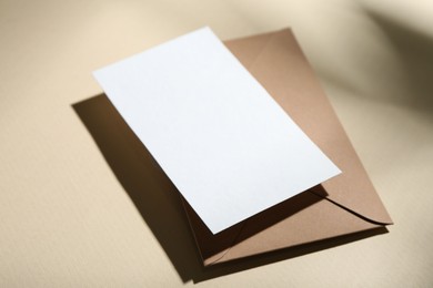 Photo of Blank greeting card and paper envelope on beige background, closeup