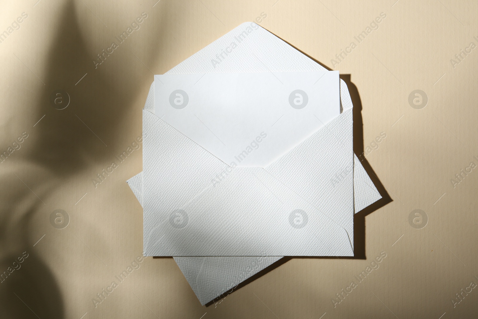 Photo of Blank greeting card and paper envelopes on beige background, top view