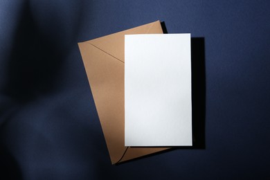 Photo of Blank greeting card and paper envelope on dark blue background, top view
