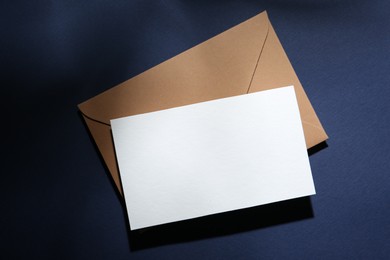 Photo of Blank greeting card and paper envelope on dark blue background, top view