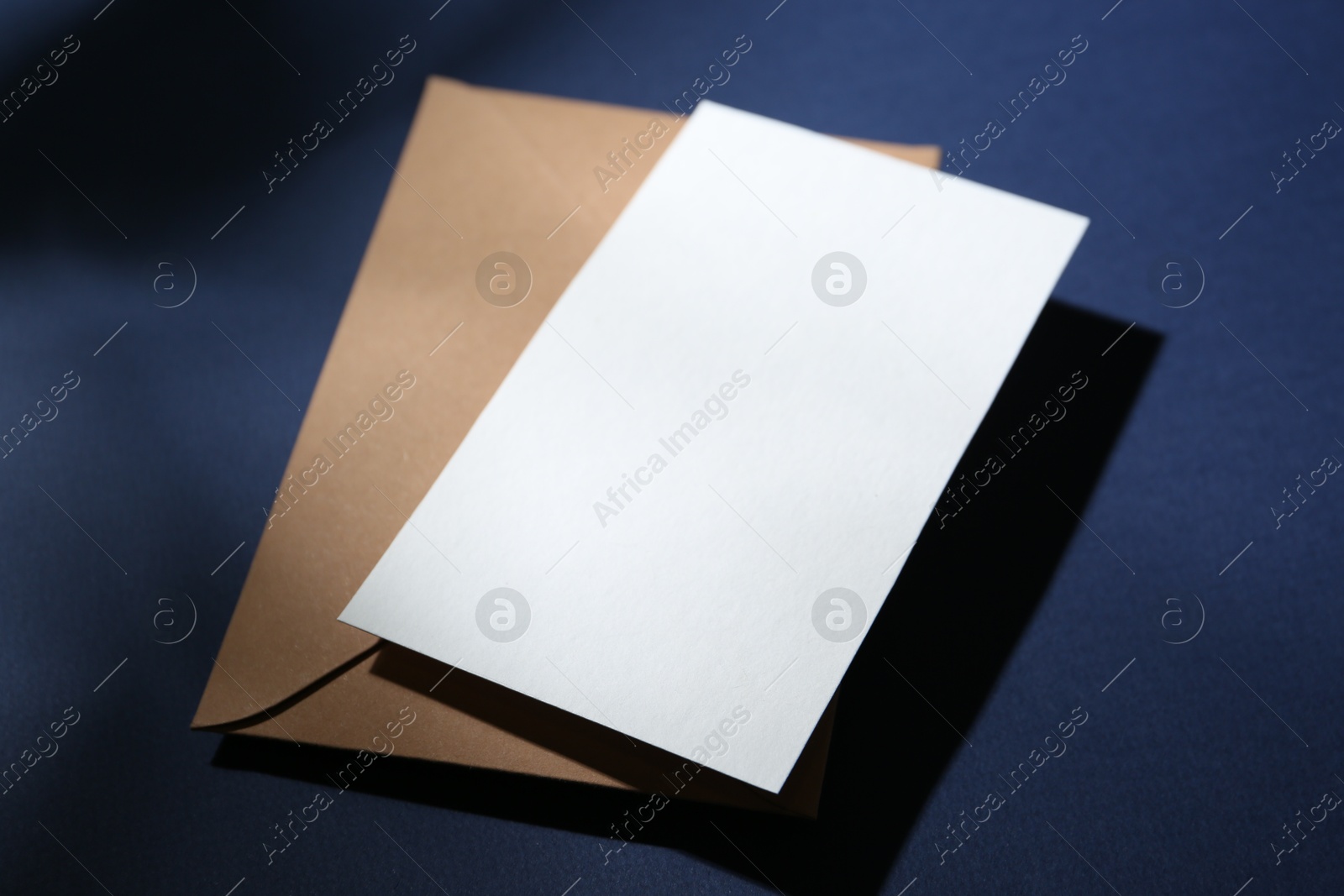 Photo of Blank greeting card and paper envelope on dark blue background, closeup