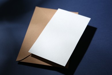Photo of Blank greeting card and paper envelope on dark blue background, closeup