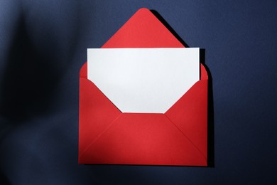 Photo of Blank greeting card in red paper envelope on dark blue background, top view