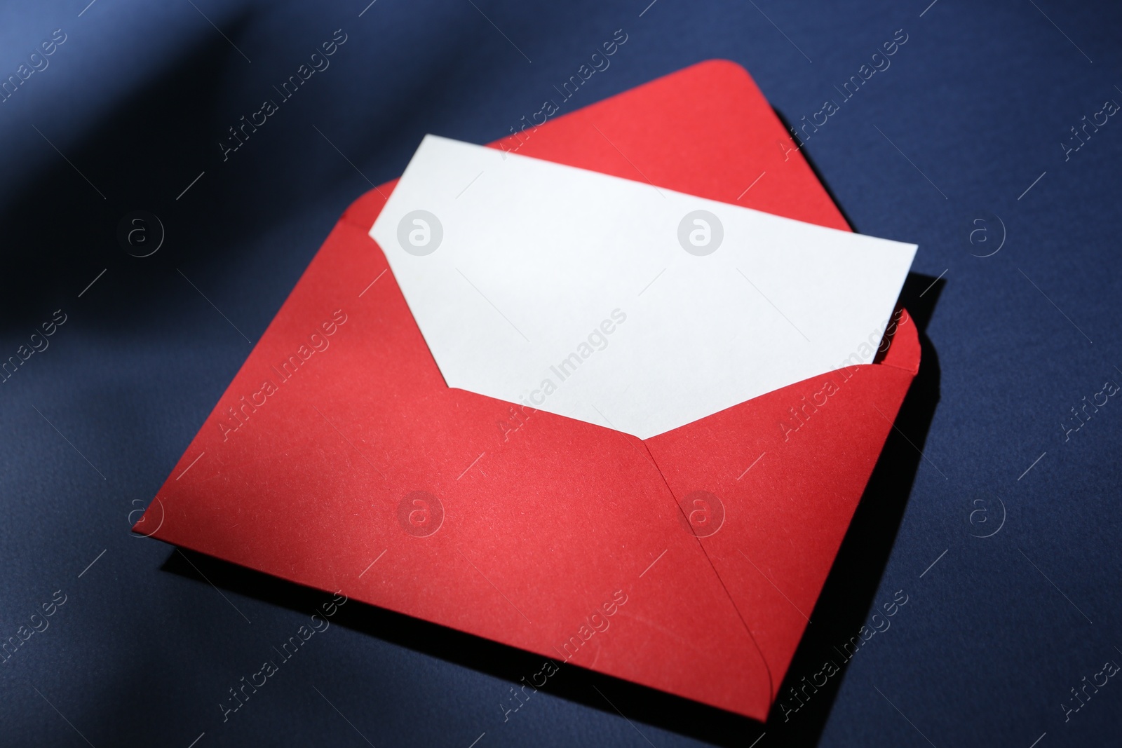 Photo of Blank greeting card in red paper envelope on dark blue background, closeup