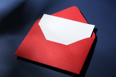Photo of Blank greeting card in red paper envelope on dark blue background, closeup