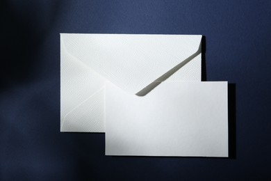 Photo of Blank greeting card and paper envelope on dark blue background, top view