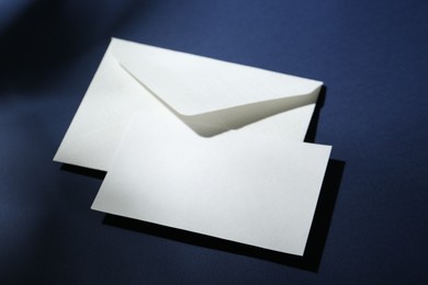 Photo of Blank greeting card and paper envelope on dark blue background, closeup