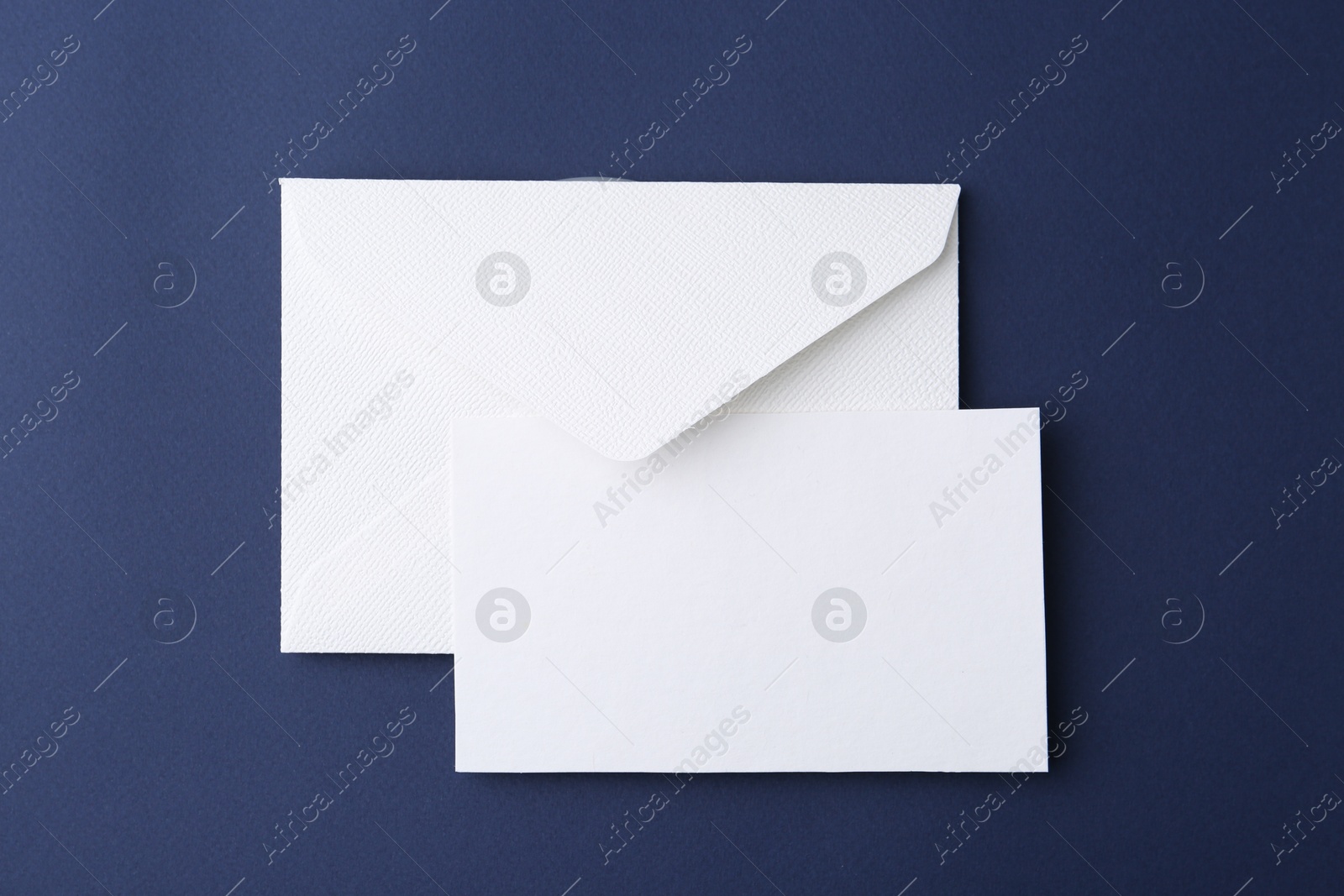 Photo of Blank greeting card and paper envelope on dark blue background, top view
