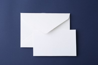 Photo of Blank greeting card and paper envelope on dark blue background, top view