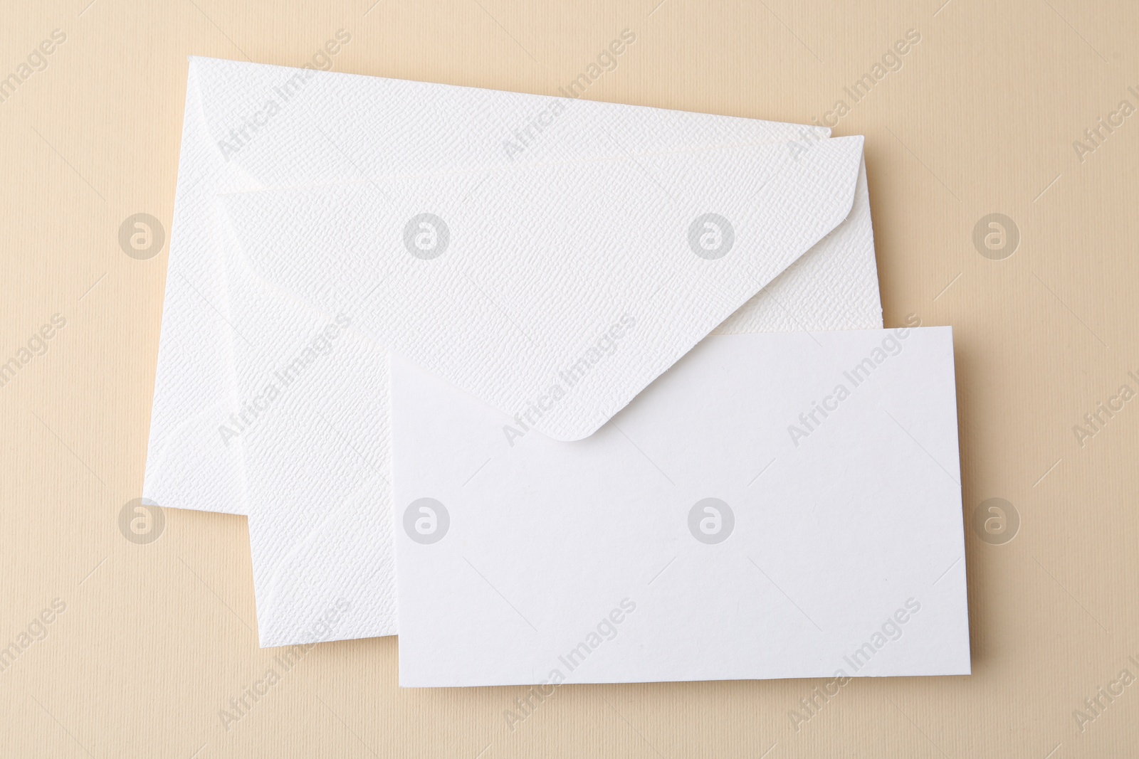 Photo of Blank greeting card and envelopes on beige background, top view