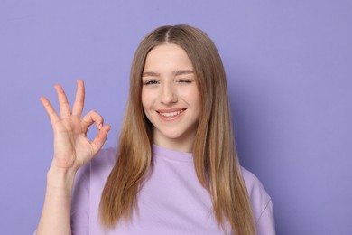 Photo of Portrait of smiling teenage girl showing ok gesture on violet background