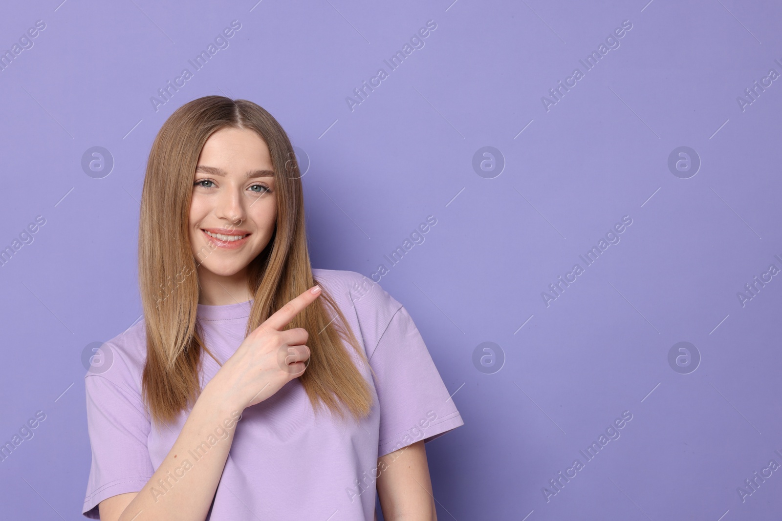 Photo of Portrait of smiling teenage girl pointing at something on violet background. Space for text