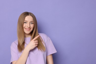 Photo of Portrait of smiling teenage girl pointing at something on violet background. Space for text