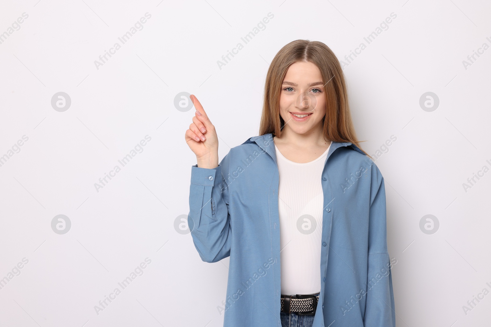 Portrait of smiling teenage girl pointing at something on white background. Space for text Photo of Portrait of smiling teenage girl pointing at something on white background. Space for text