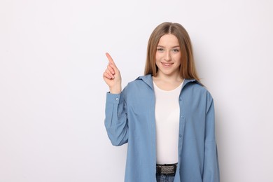 Photo of Portrait of smiling teenage girl pointing at something on white background. Space for text