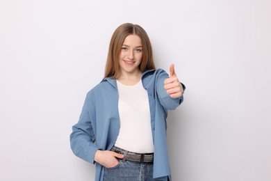 Photo of Portrait of smiling teenage girl showing thumbs up on white background