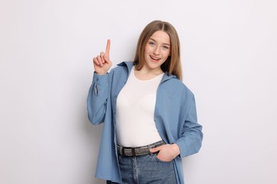 Photo of Portrait of smiling teenage girl pointing upwards on white background