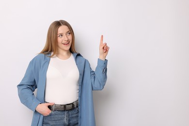 Photo of Portrait of smiling teenage girl pointing upwards on white background. Space for text