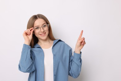 Photo of Portrait of smiling teenage girl pointing at something on white background. Space for text