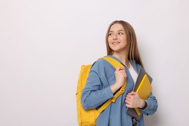 Photo of Smiling teenage girl with books and backpack on white background. Space for text