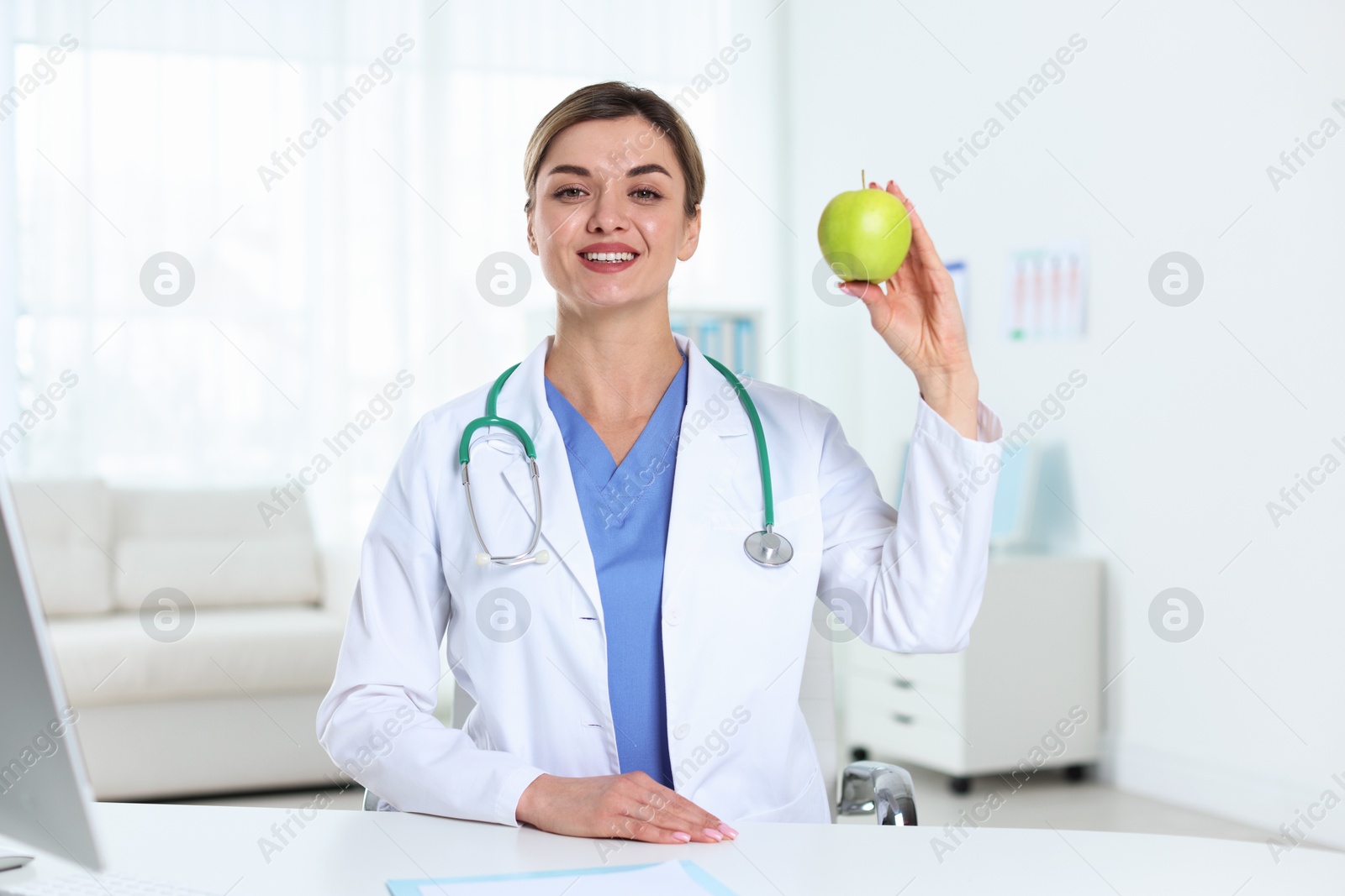 Nutritionist with green apple and stethoscope at table in clinic Photo of Nutritionist with green apple and stethoscope at table in clinic