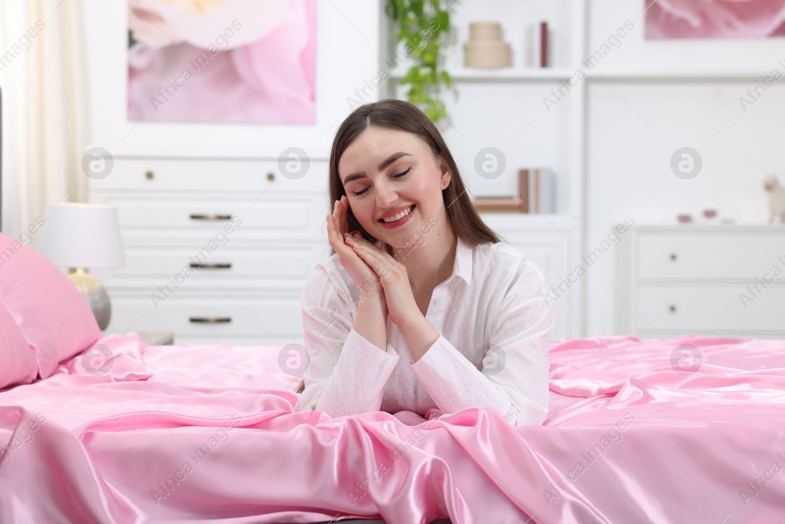 Smiling woman on bed with pink silk linens indoors Photo of Smiling woman on bed with pink silk linens indoors