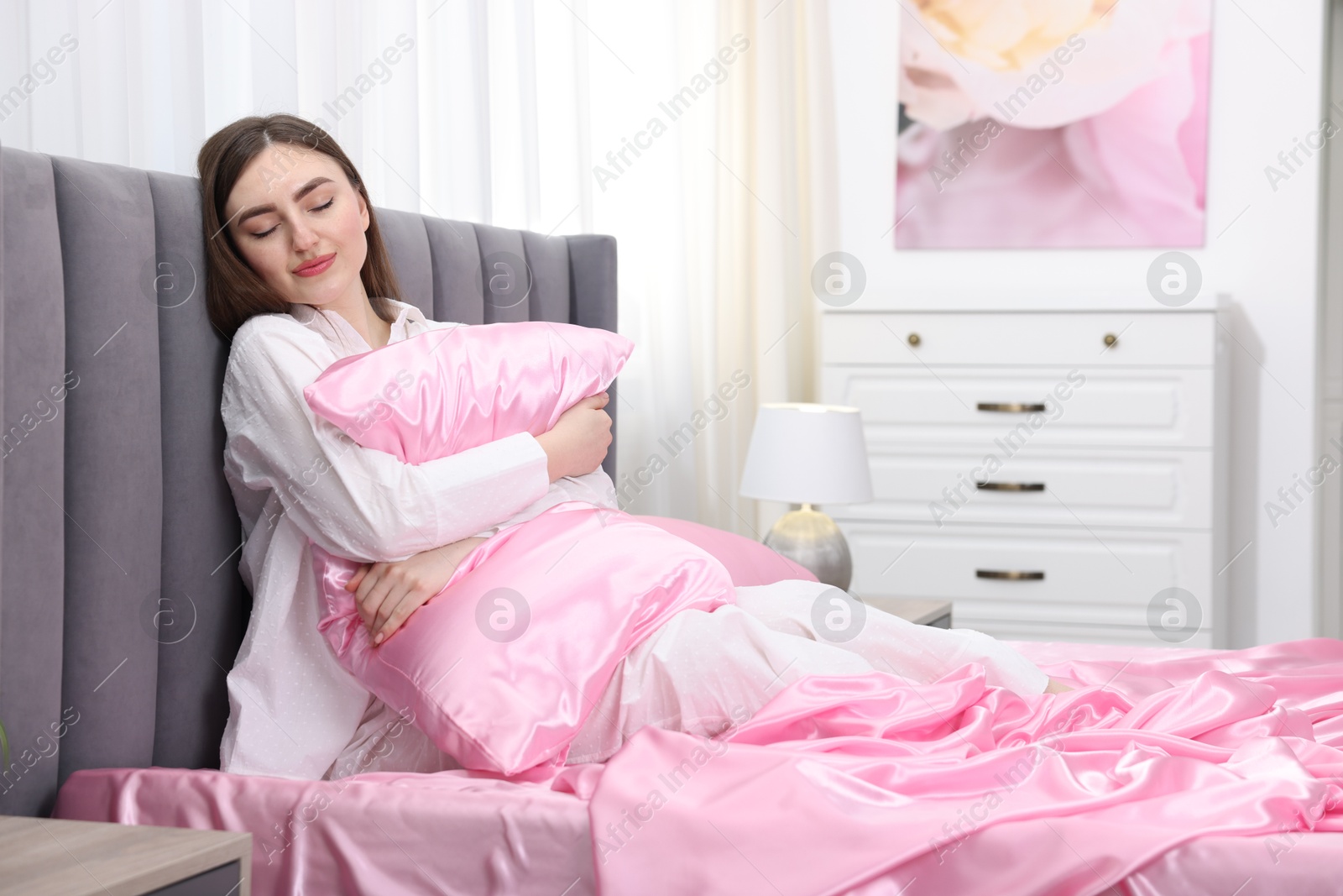 Woman hugging pillow on bed with pink silk linens indoors Photo of Woman hugging pillow on bed with pink silk linens indoors