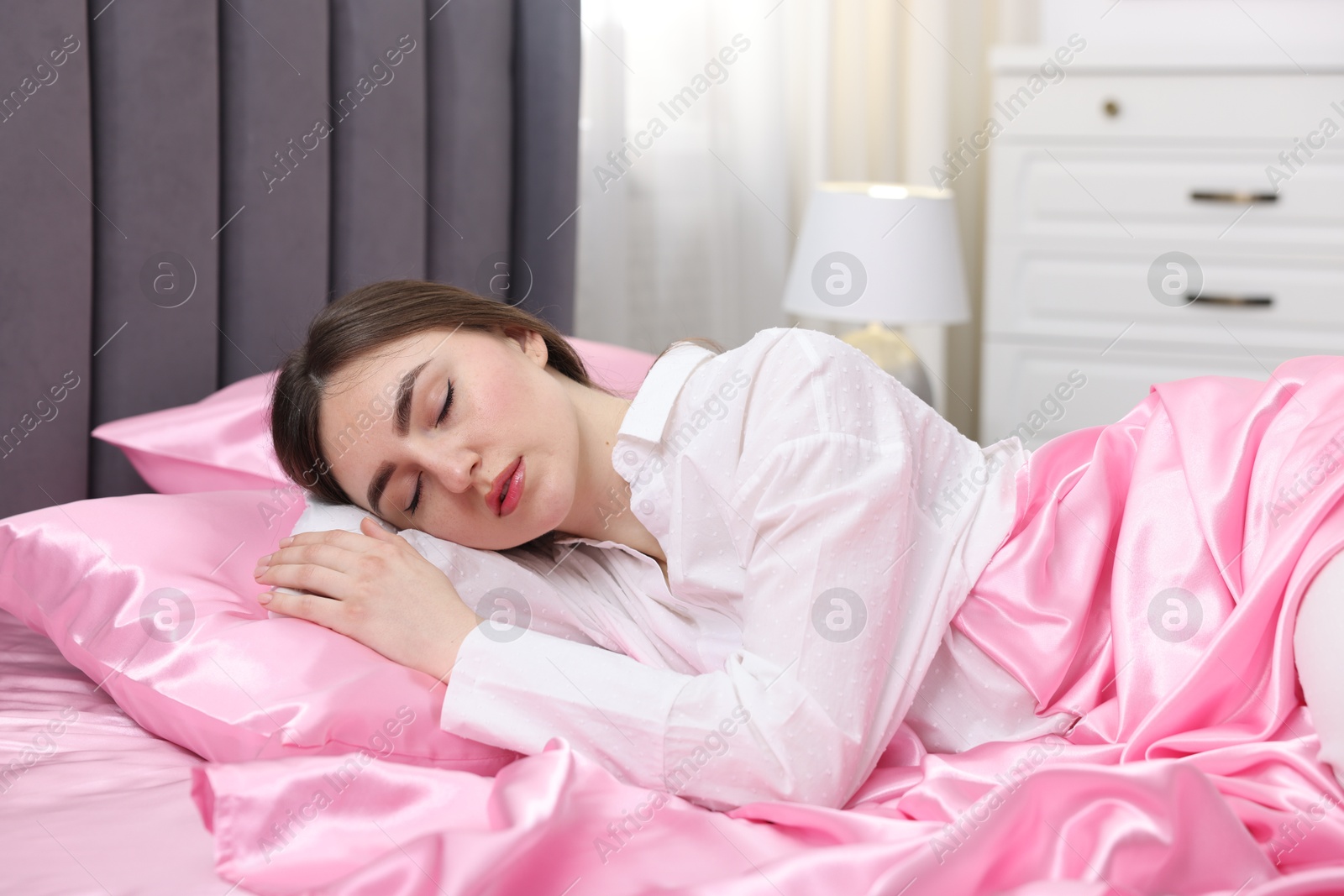 Woman sleeping in bed with pink silk linens indoors Photo of Woman sleeping in bed with pink silk linens indoors