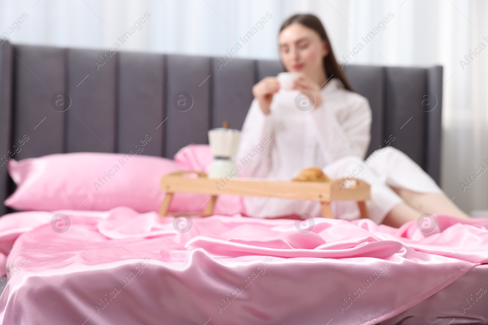 Woman drinking coffee on bed with pink silk linens indoors, selective focus Photo of Woman drinking coffee on bed with pink silk linens indoors, selective focus